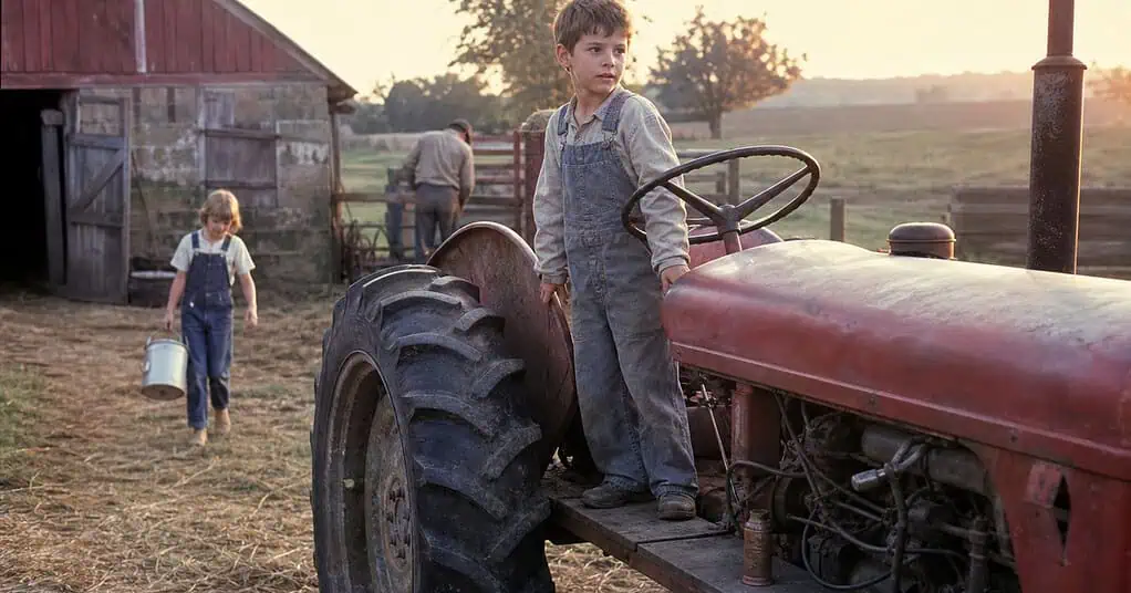 Farm children helping with morning chores beside a tractor and barn in the late 1960s