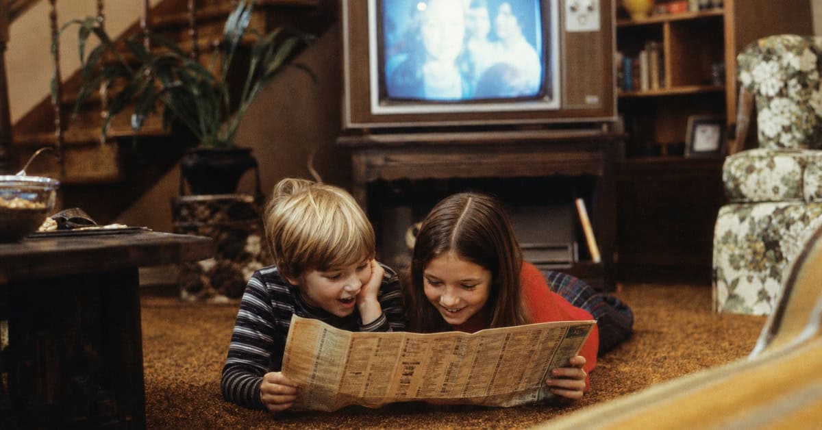 Siblings studying weekend television listings for cartoon previews in the 1970s