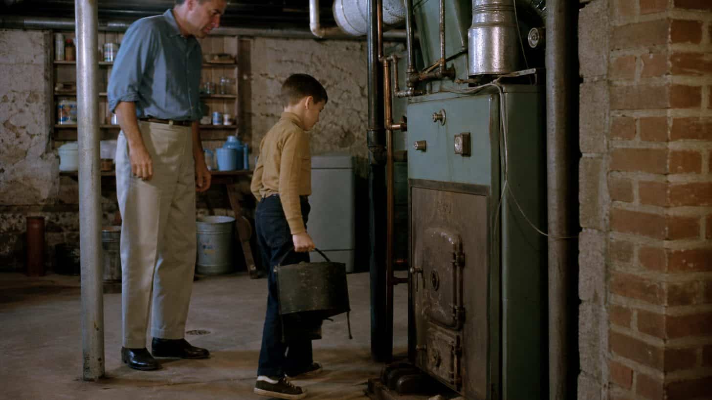 Child carrying coal to a basement furnace under adult supervision in the early 1960s