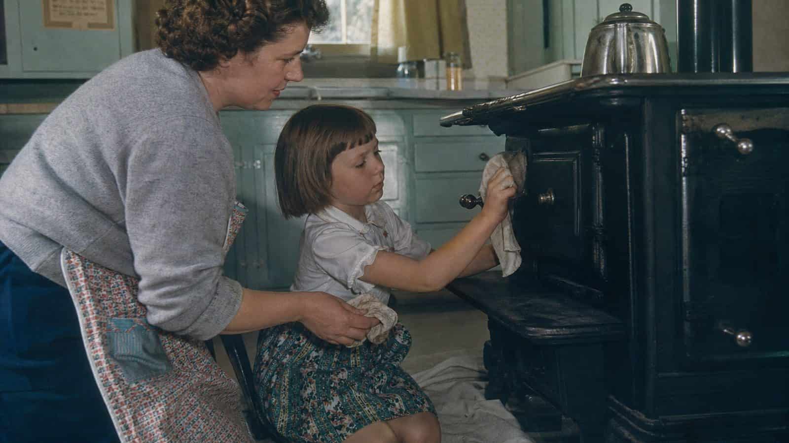 Child learning to polish a cast-iron stove in an early-1960s kitchen