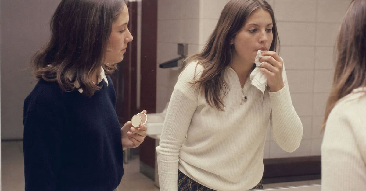Teenage girl removing lipstick at a late-1960s school mirror