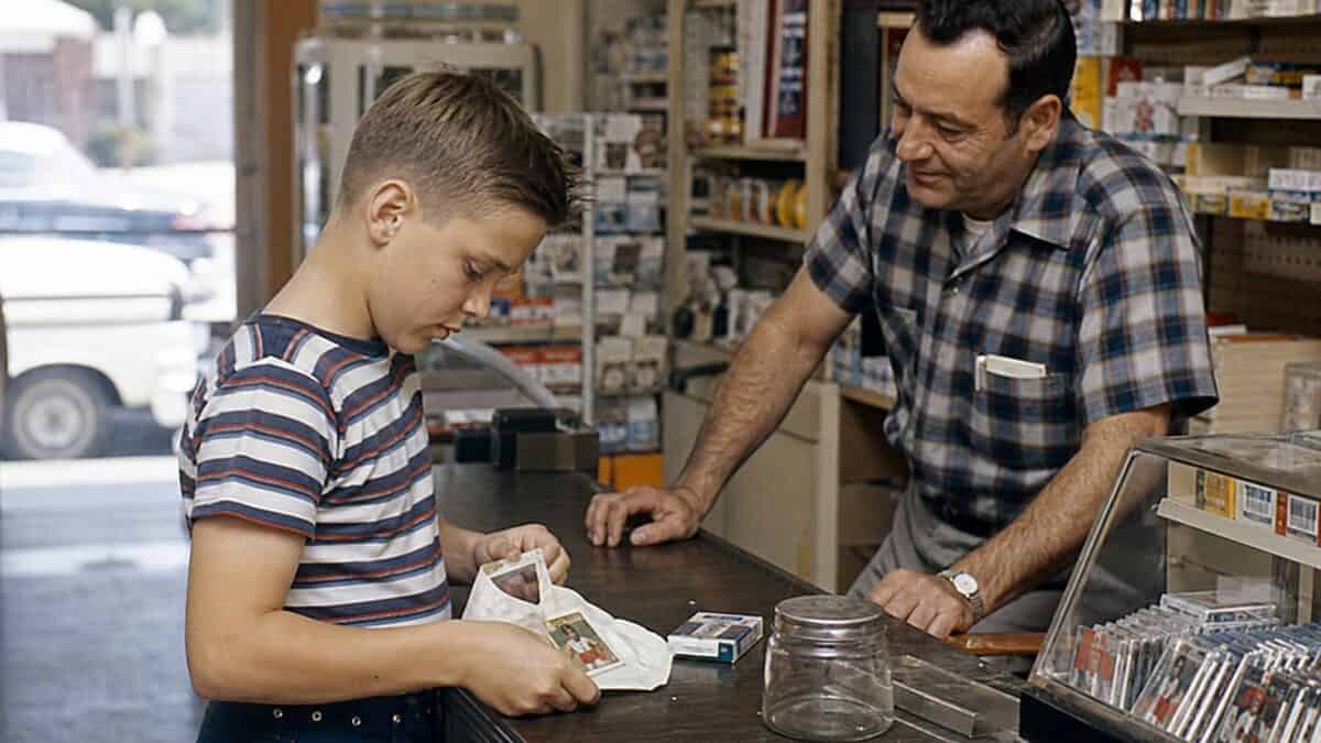 14 Things You Could Buy for a Nickel in 1960 (That Cost $20+ Now) 8 Child opening a pack of baseball cards at a store counter in 1960