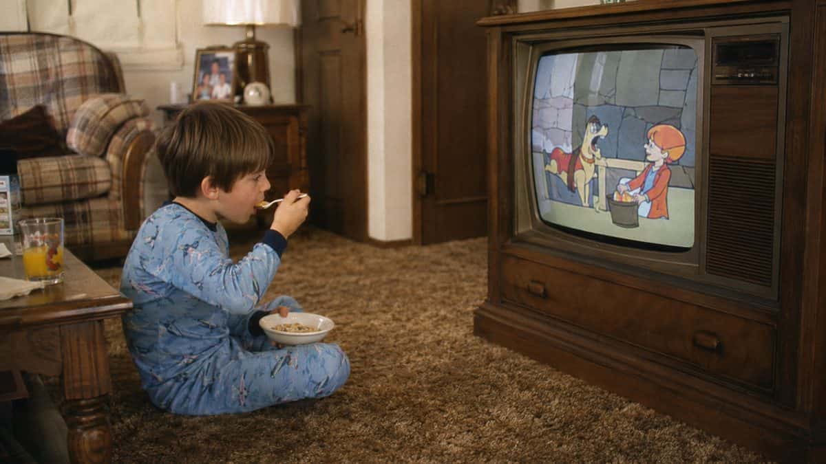 Kid in pajamas eating cereal in front of a TV