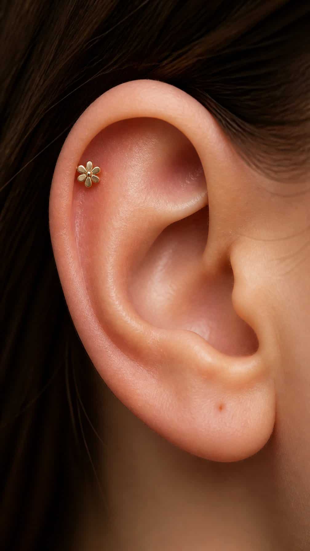 Close-up of an ear with a small flower stud piercing on the upper cartilage.