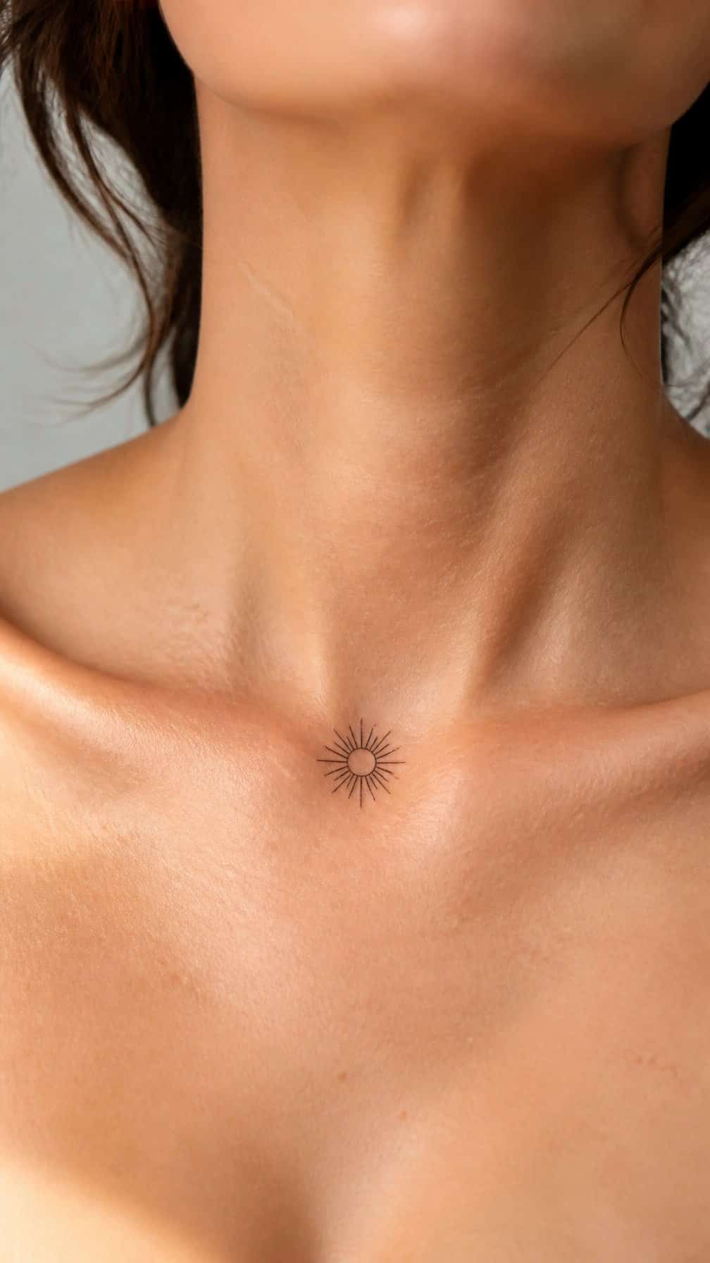 A person’s upper chest showing a tiny sunburst tattoo centered on the collarbone.
