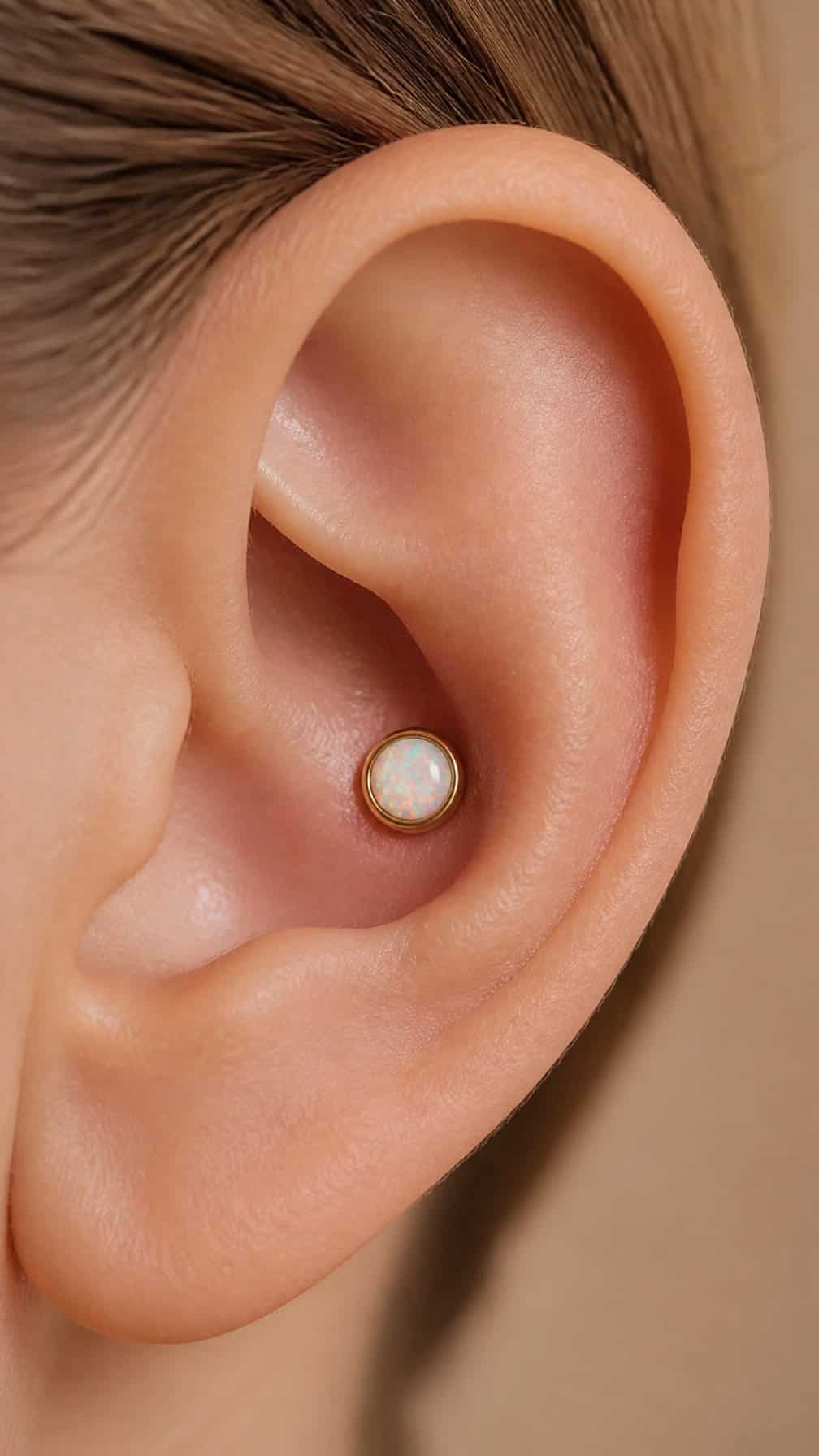 Close-up of an ear wearing a tiny yellow-gold bezel-set opal conch piercing.