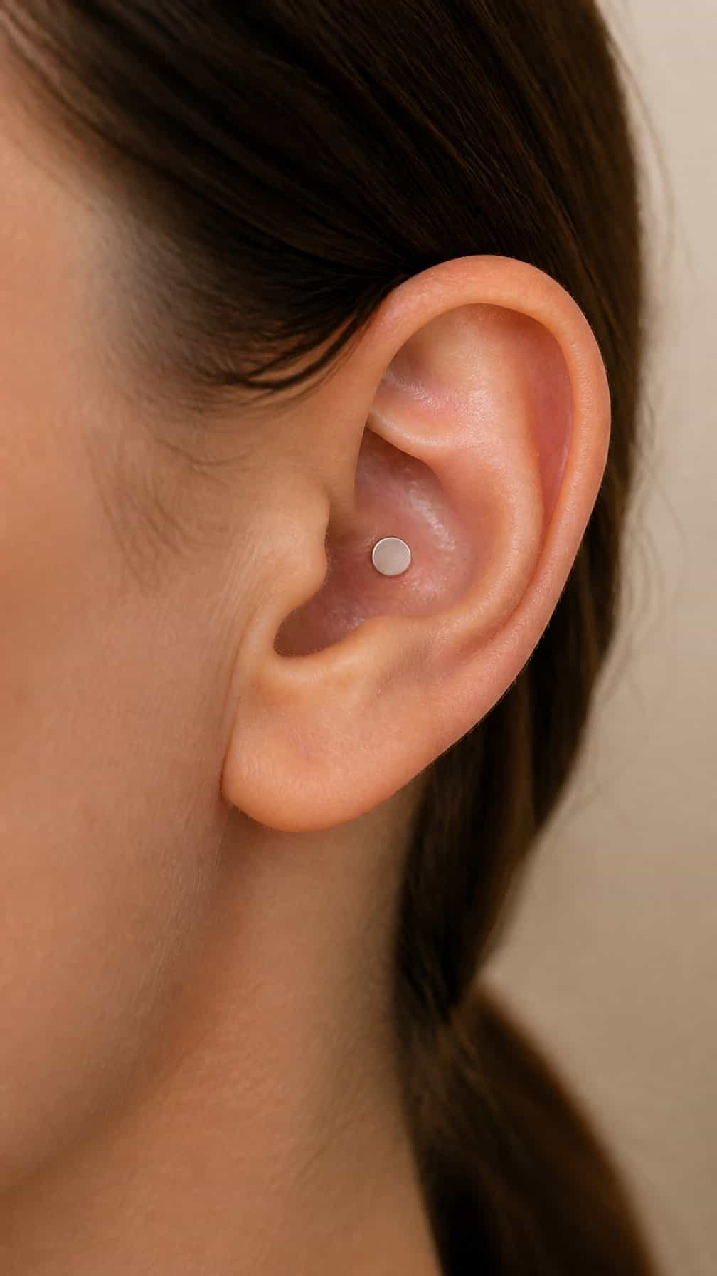Close-up of an ear with a small titanium flat-back conch labret piercing.