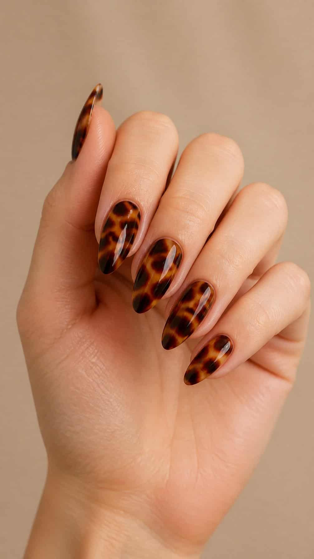 A hand with long almond-shaped tortoiseshell-patterned nails.