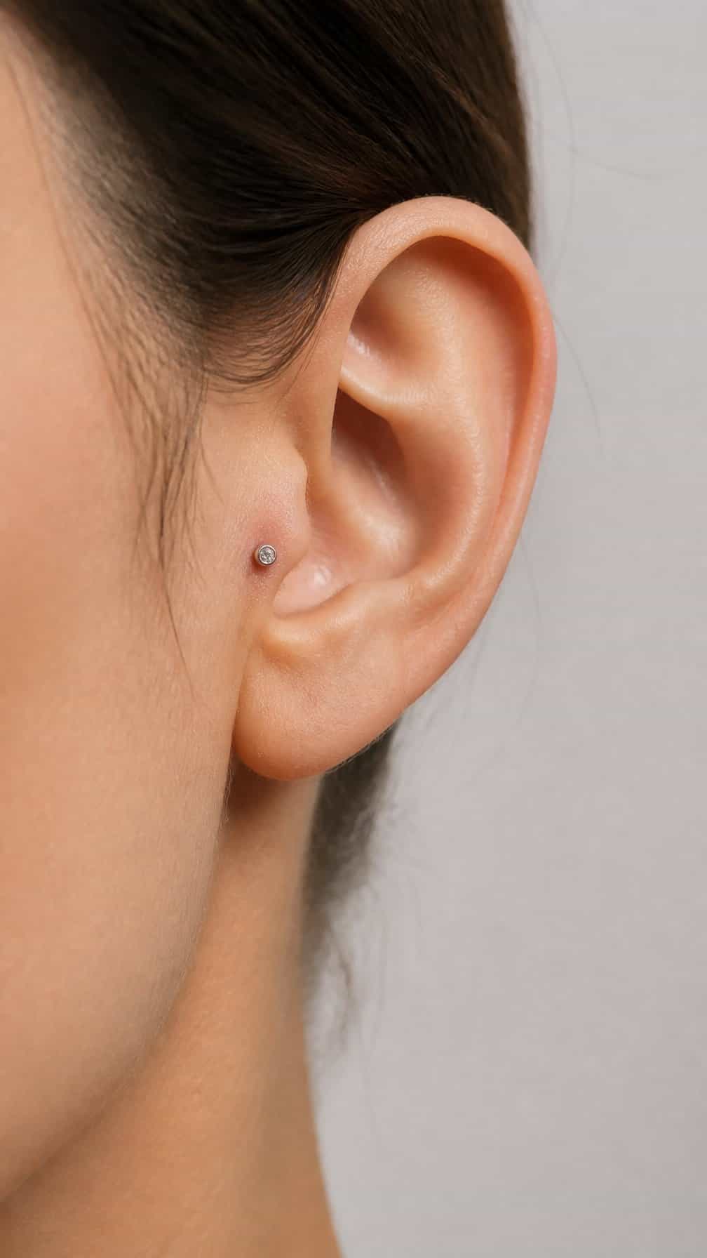 Close-up side view of an ear with a small flat-back stud in the tragus.