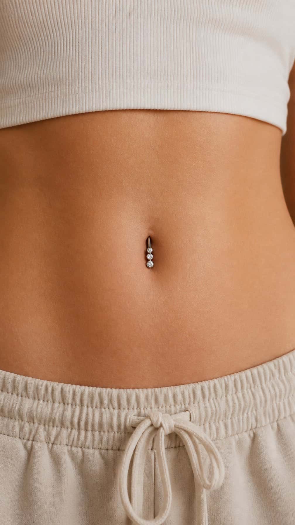 Close-up of an adult person’s midriff featuring a navel piercing with three gemstones on a curved bar.