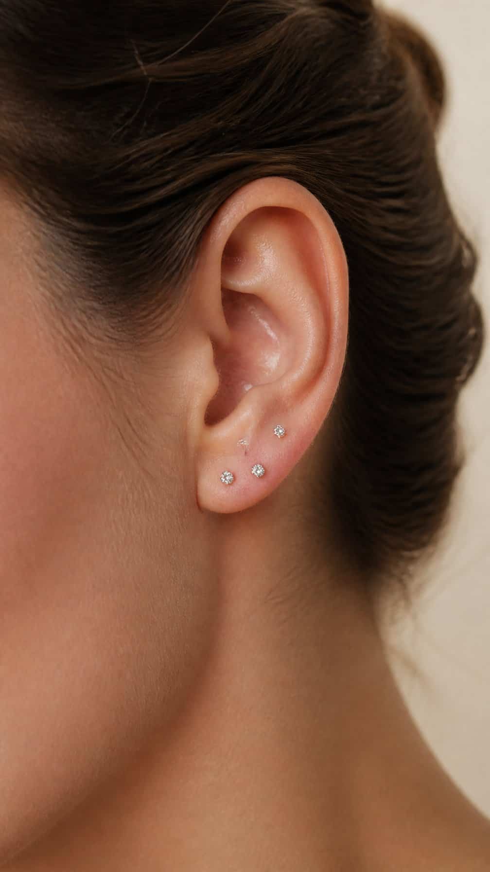 Close-up of an ear with three small stud earrings arranged in a constellation pattern across the upper lobe.