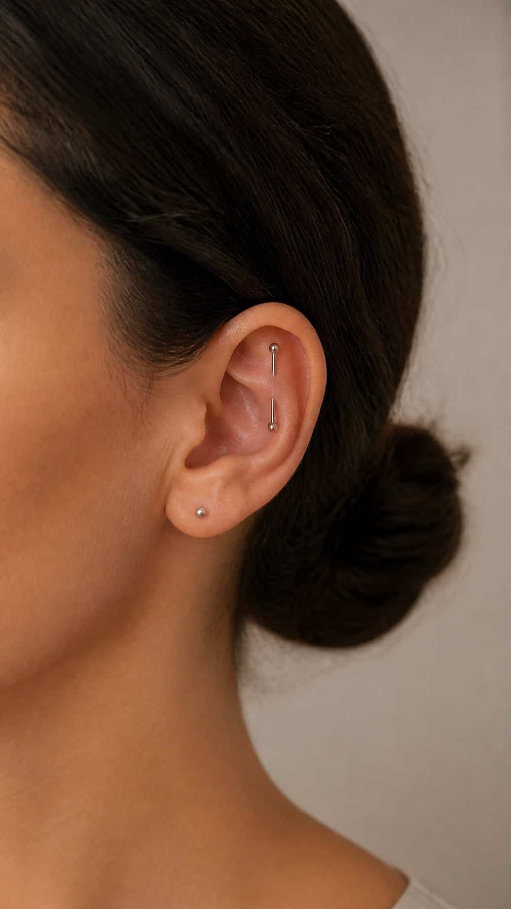 Close-up of an adult ear featuring a vertical industrial barbell piercing.