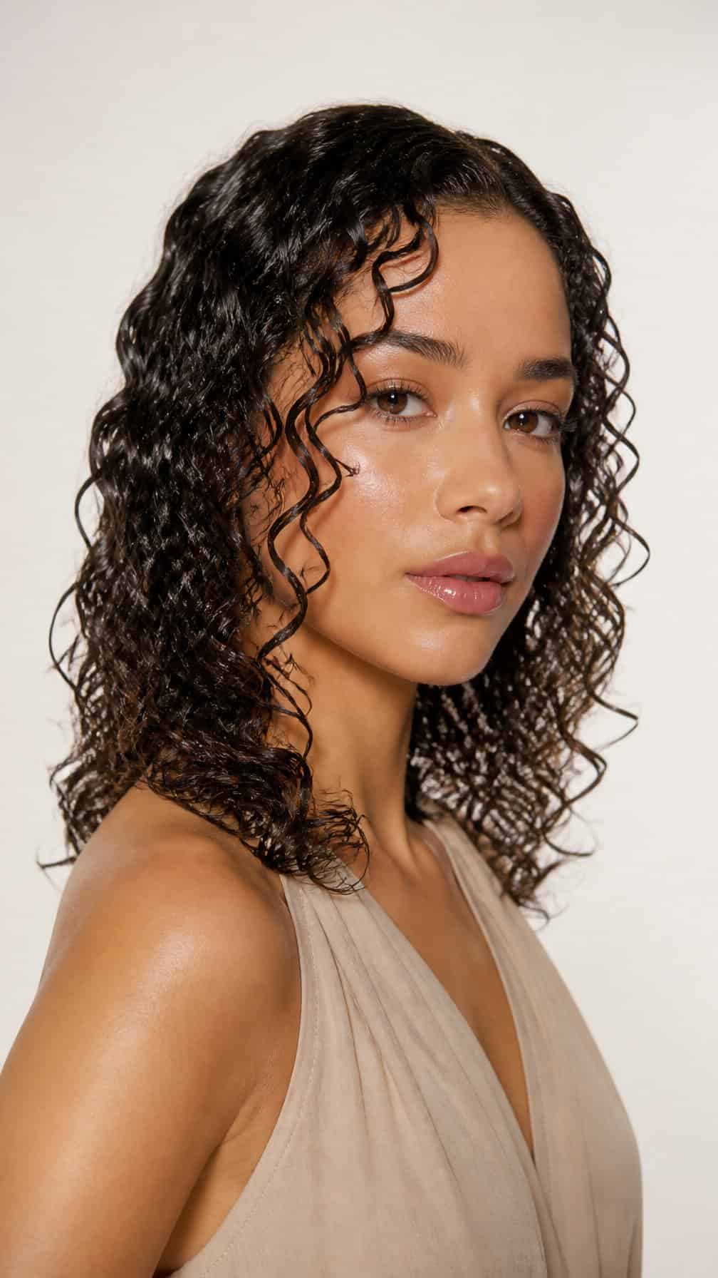 A person with glossy, defined curly hair poses against a plain light background.