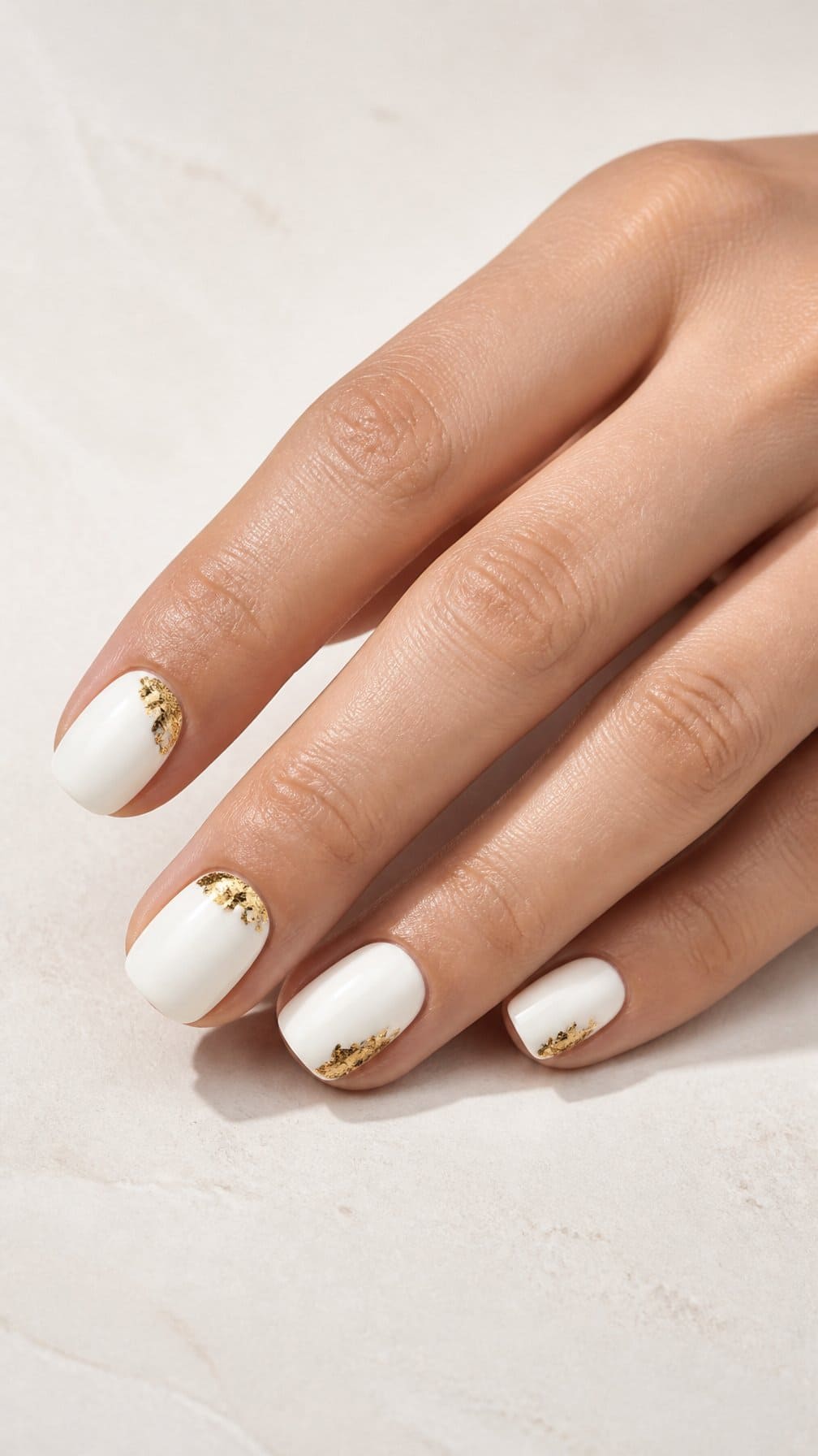 A manicured hand with glossy white nails featuring delicate gold foil accents.