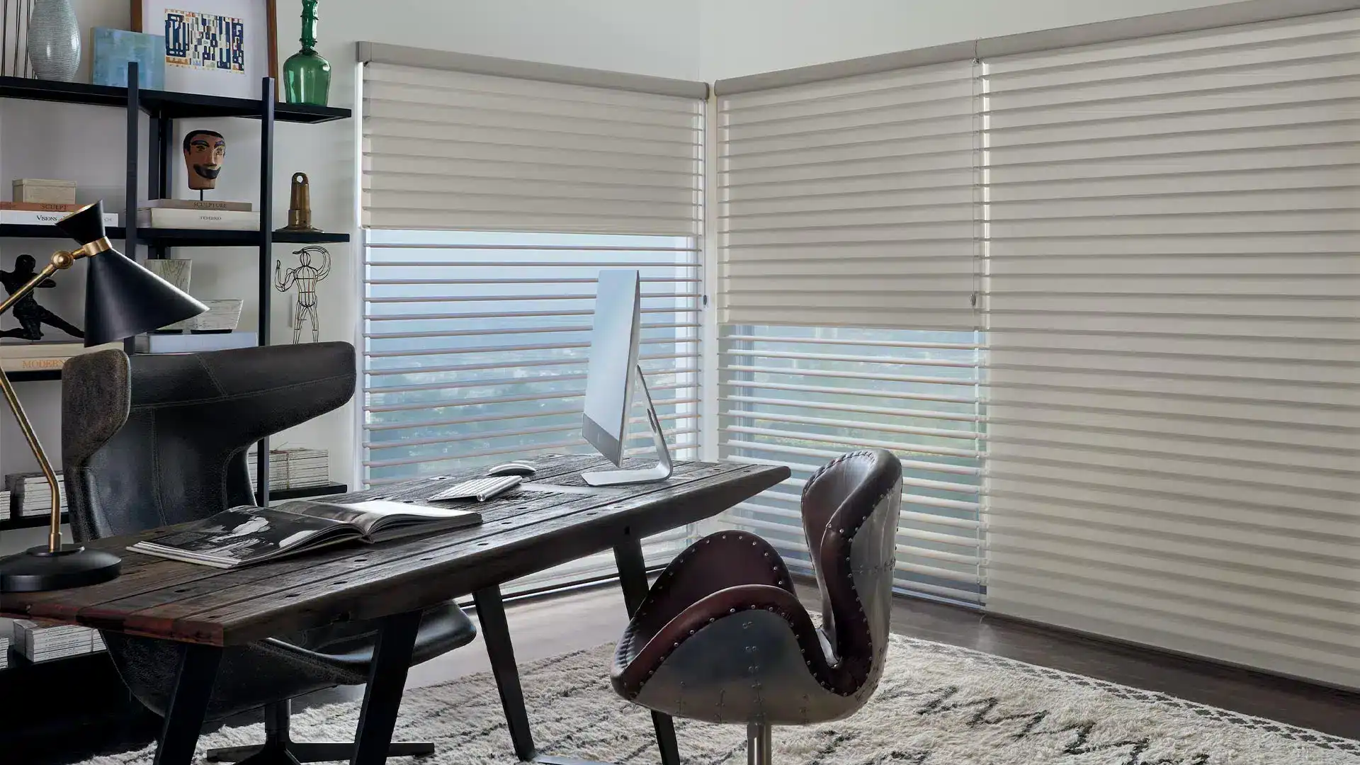 Stylish home office featuring a wooden desk, ergonomic chair, and large windows with blinds providing natural lighting. Includes decorative elements on shelves, creating a cozy workspace suitable for remote work or studying.