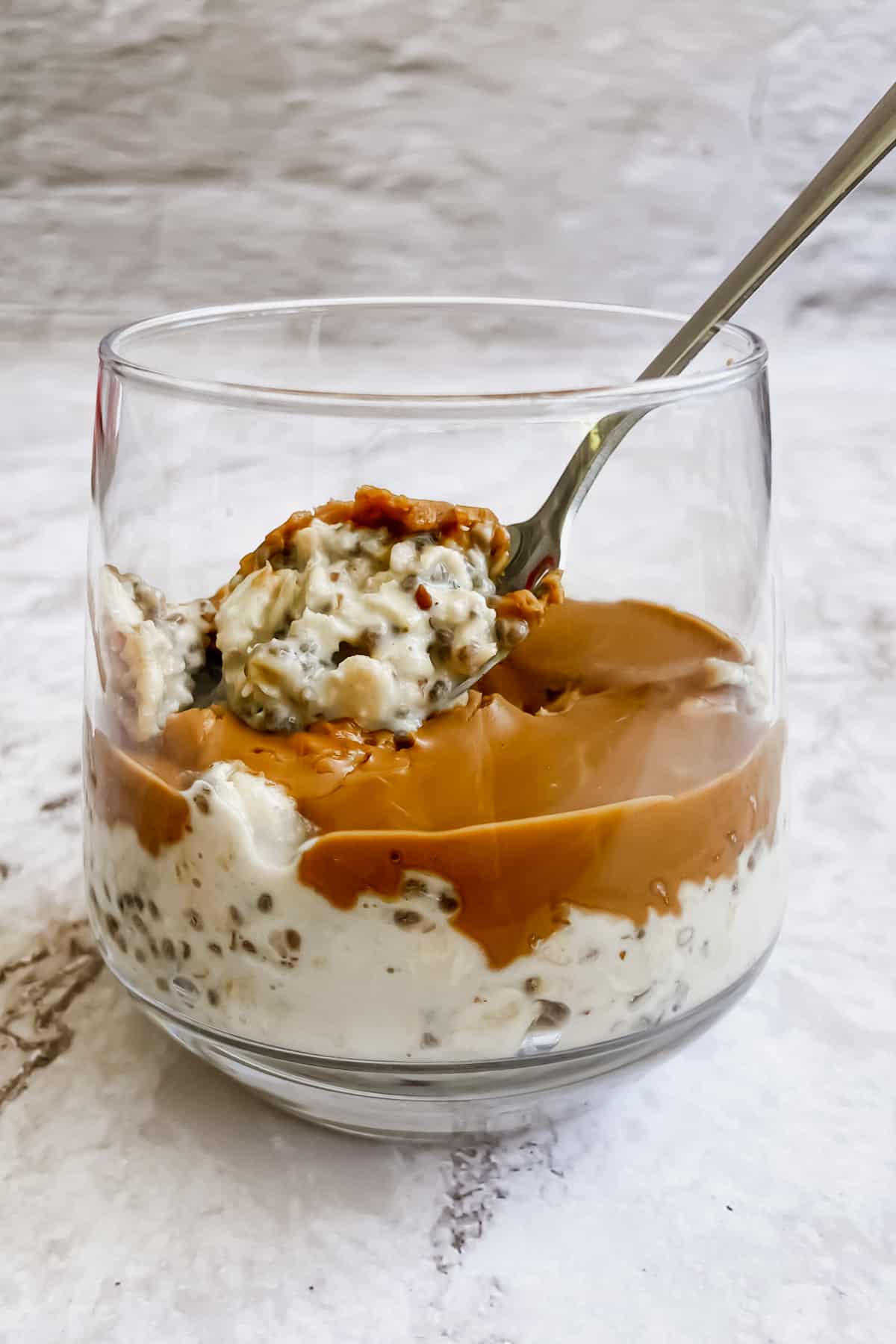 A spoon resting in a glass of overnight oats against a white background.