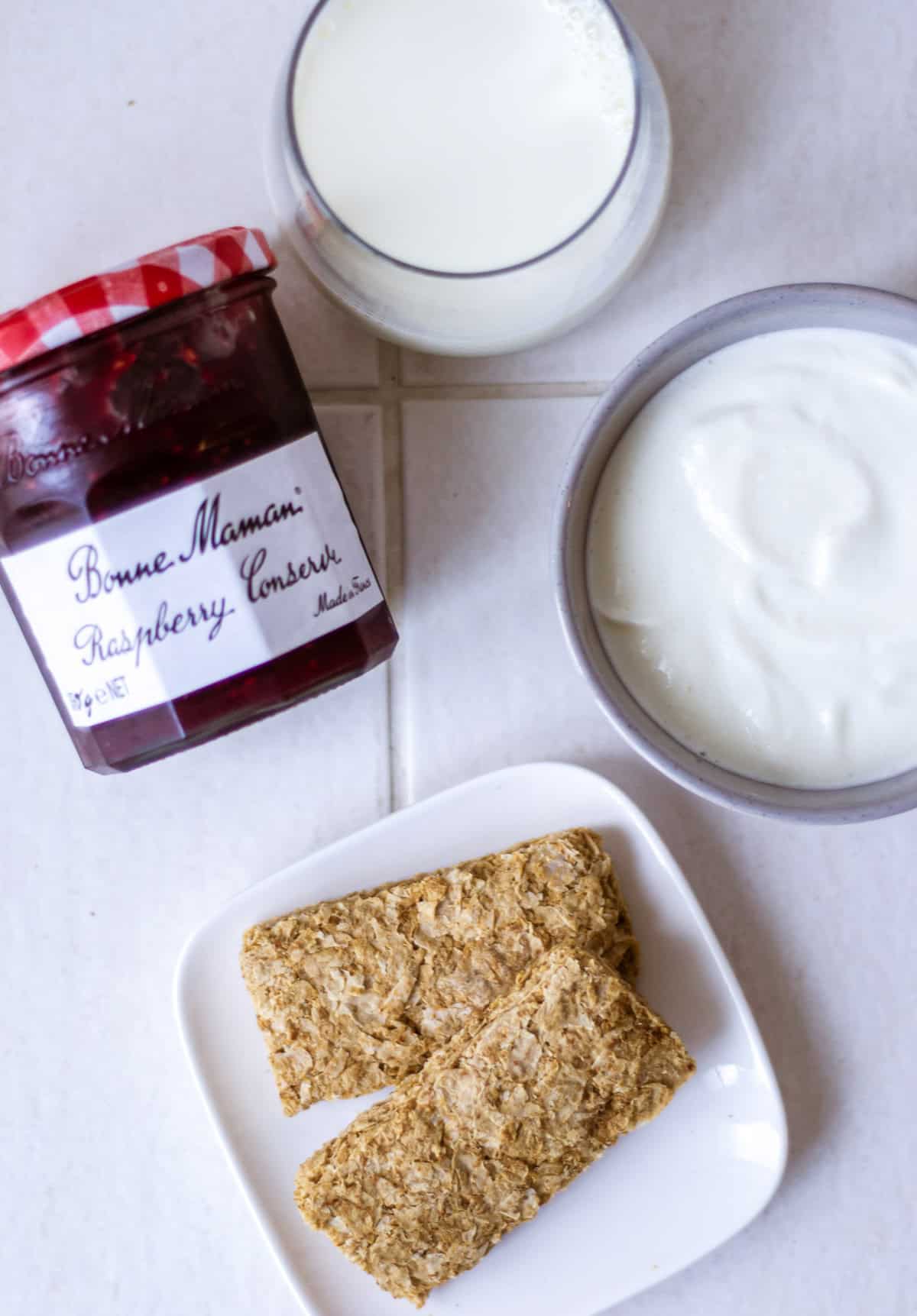 Overhead shot of ingredients for cheesecake overnight Weetabix, counter clockwise starting from the top: milk, Greek yoghurt, weetbix/wheetabix, raspberry jam.
