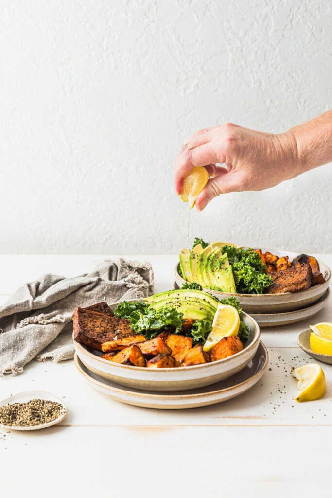 Front view of a hand squeezing even more lemon juice over the top of a sweet potato tofu nourish bowl.