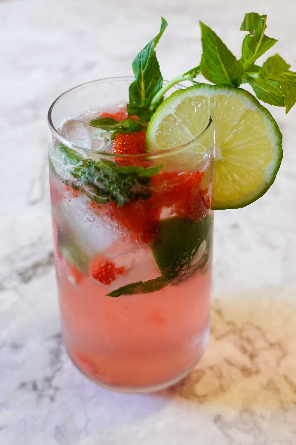 Photo of a virgin strawberry mojito in a tall glass, garnished with a mint sprig and lime slice.