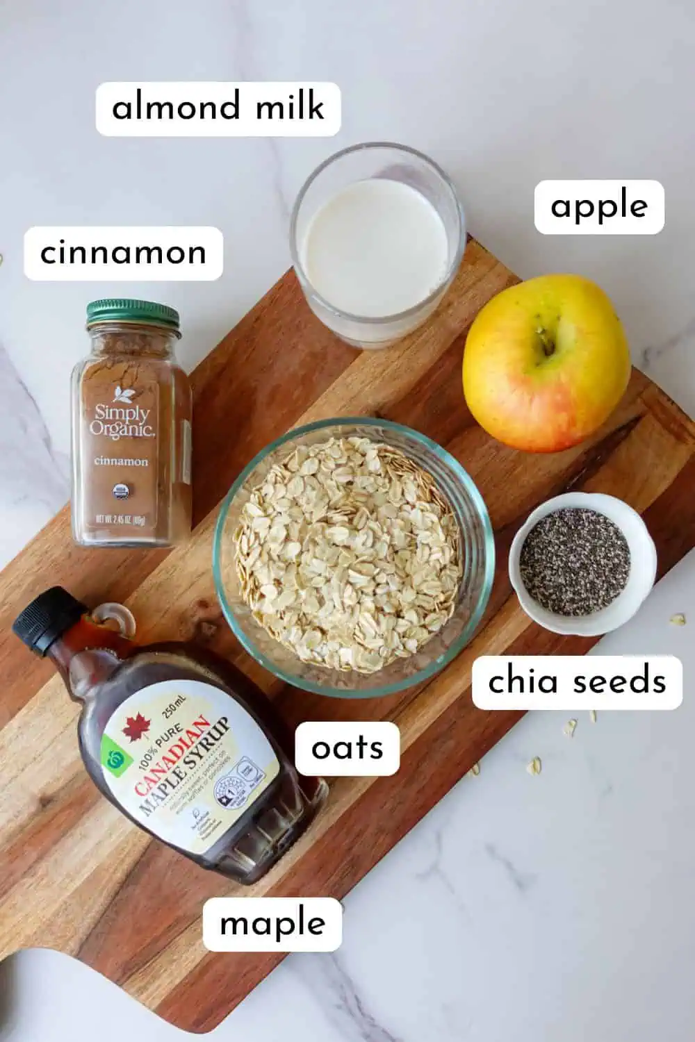 Flatlay of apple porridge ingredients, labelled, including: cinnamon, almond milk, apple, chia seeds, oats, maple and cinnamon.