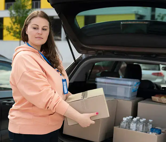 Woman loading a cardboard box into a vehicle during a commercial move, with organized supplies and bottled water visible in the car's trunk, highlighting Smart Penny Moving's attention to detail and professionalism.