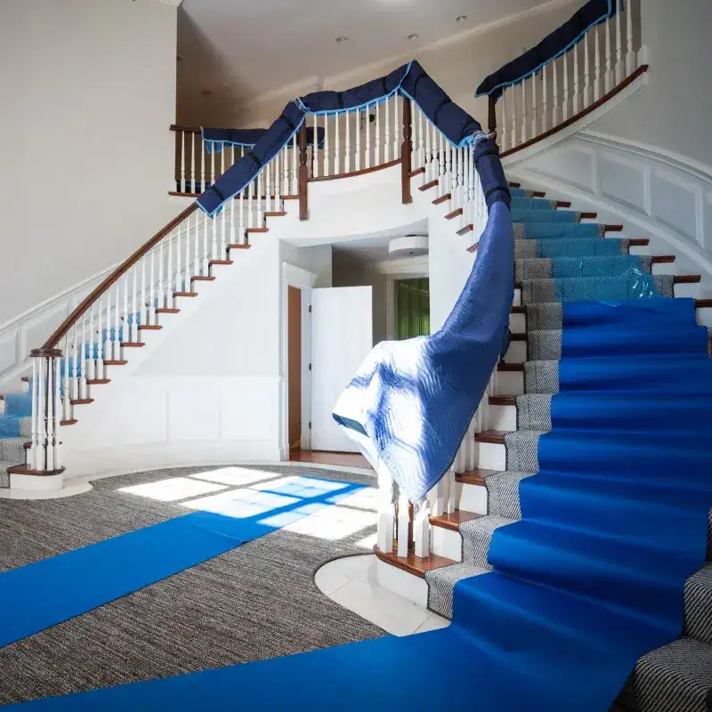 Staircase with blue moving blankets and runners protecting floors and banisters during a home move, showcasing careful preparation for safeguarding belongings.