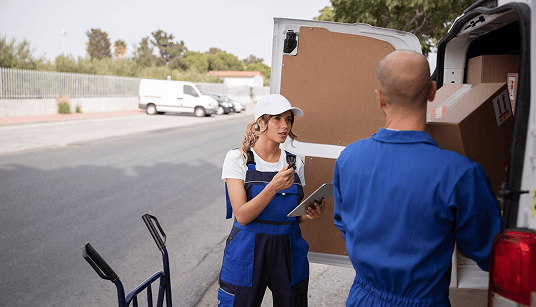 Woman in blue overalls and cap discussing logistics with a man in blue work attire near a moving van, emphasizing efficient office relocation services by Smart Penny Moving.
