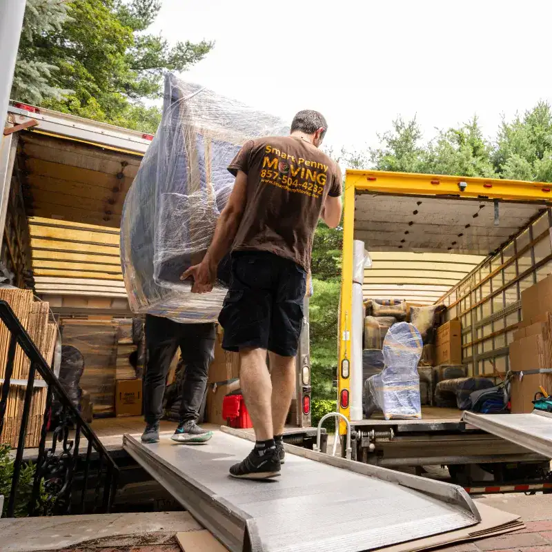 Movers from Smart Penny Moving unloading wrapped furniture from a moving truck onto a ramp, demonstrating the unloading process for a residential move.