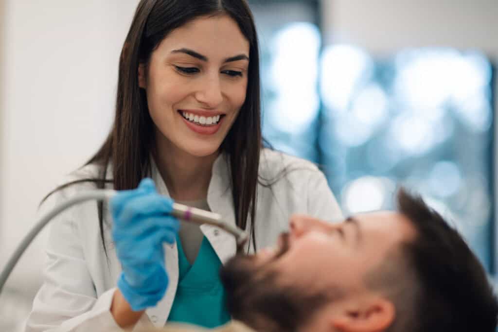 Female dentist performing dental cleaning on male patient in clinic.
