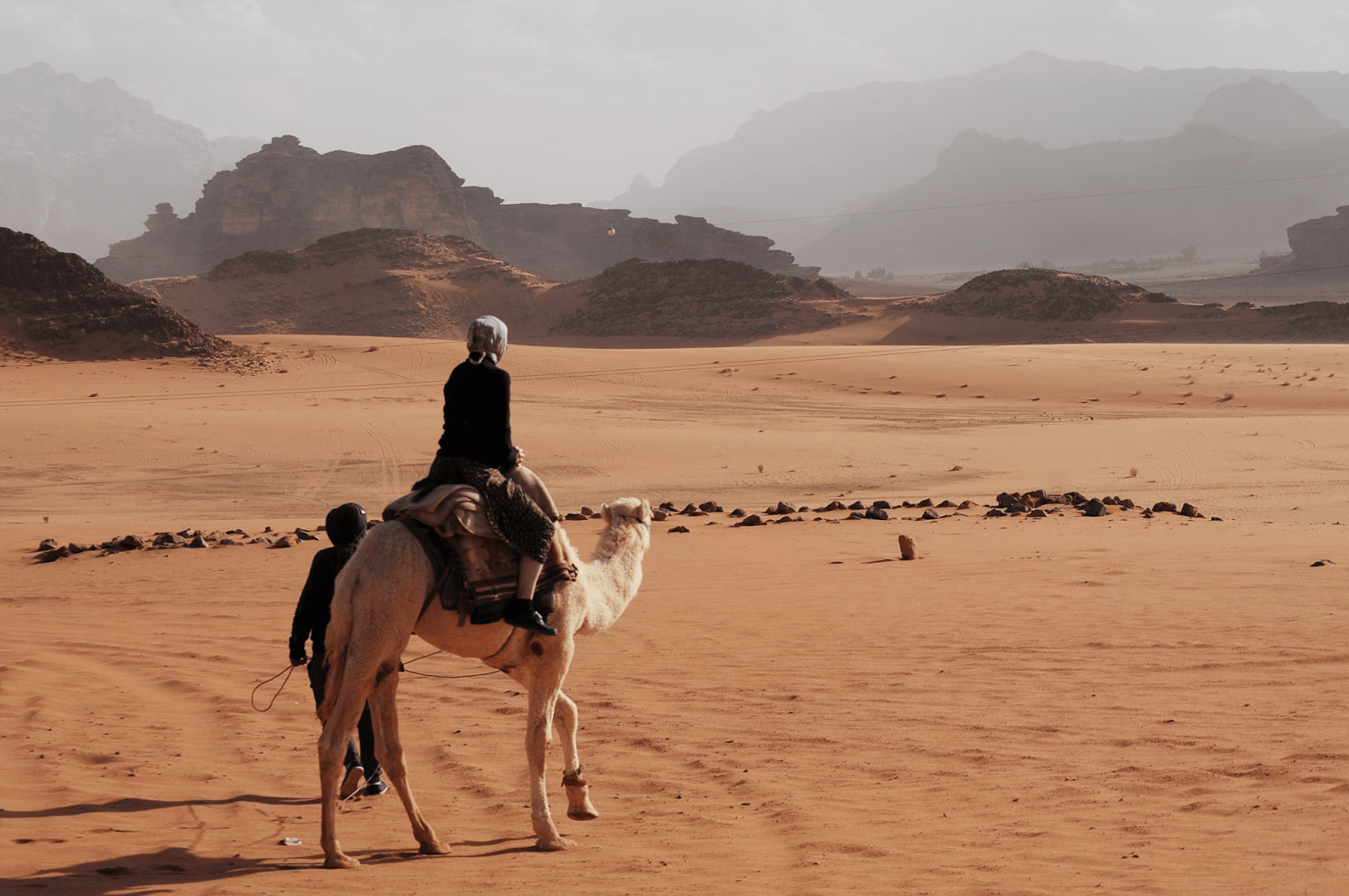 A female traveler in Saudi Arabia riding a camel in a desert - (Credits Unsplash)