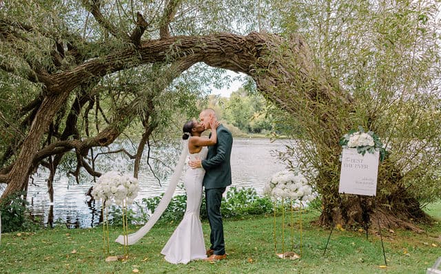 Bride and groom embracing under a willow tree archway at Riverside Park