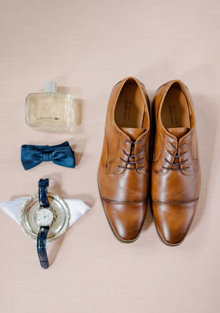 Brown leather dress shoes with watch, bow tie, perfume, and cufflinks.