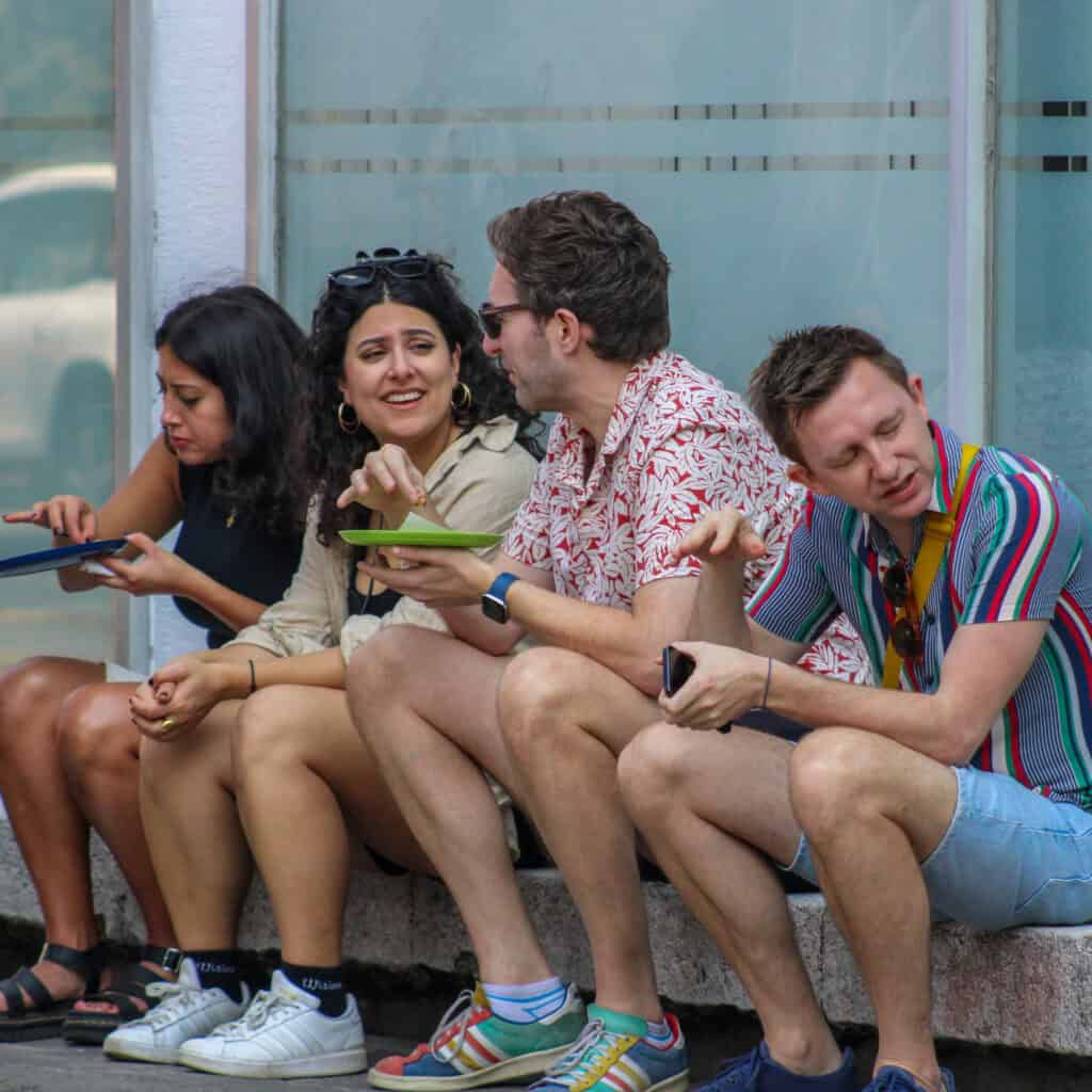 Two men and two women sitting on the sidewalk eating tacos during the Food Hood Mexico bike tour.
