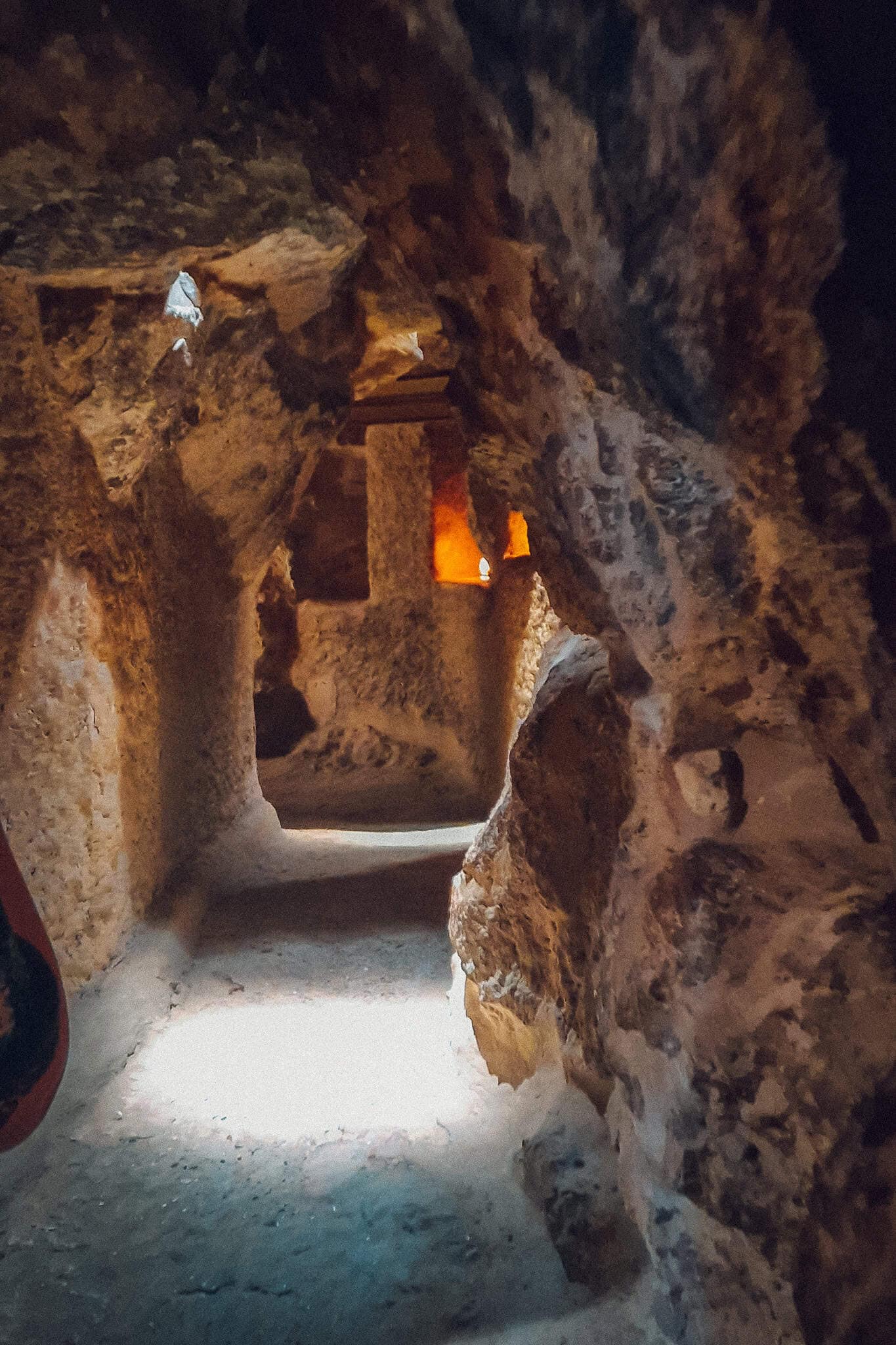 A photo of a dimly lit, rough-hewn rock tunnel leading deeper into the ancient subterranean chambers of the Giza Plateau.