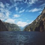 Scenic view of Milford Sound with towering cliffs and blue sky.
