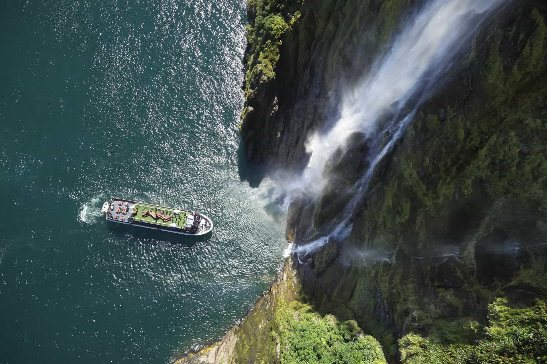 Scenic Milford Sound with waterfall and boat from above.