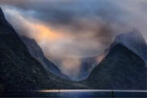Dramatic sunset over Milford Sound with towering Mitre Peak and misty rainforest.
