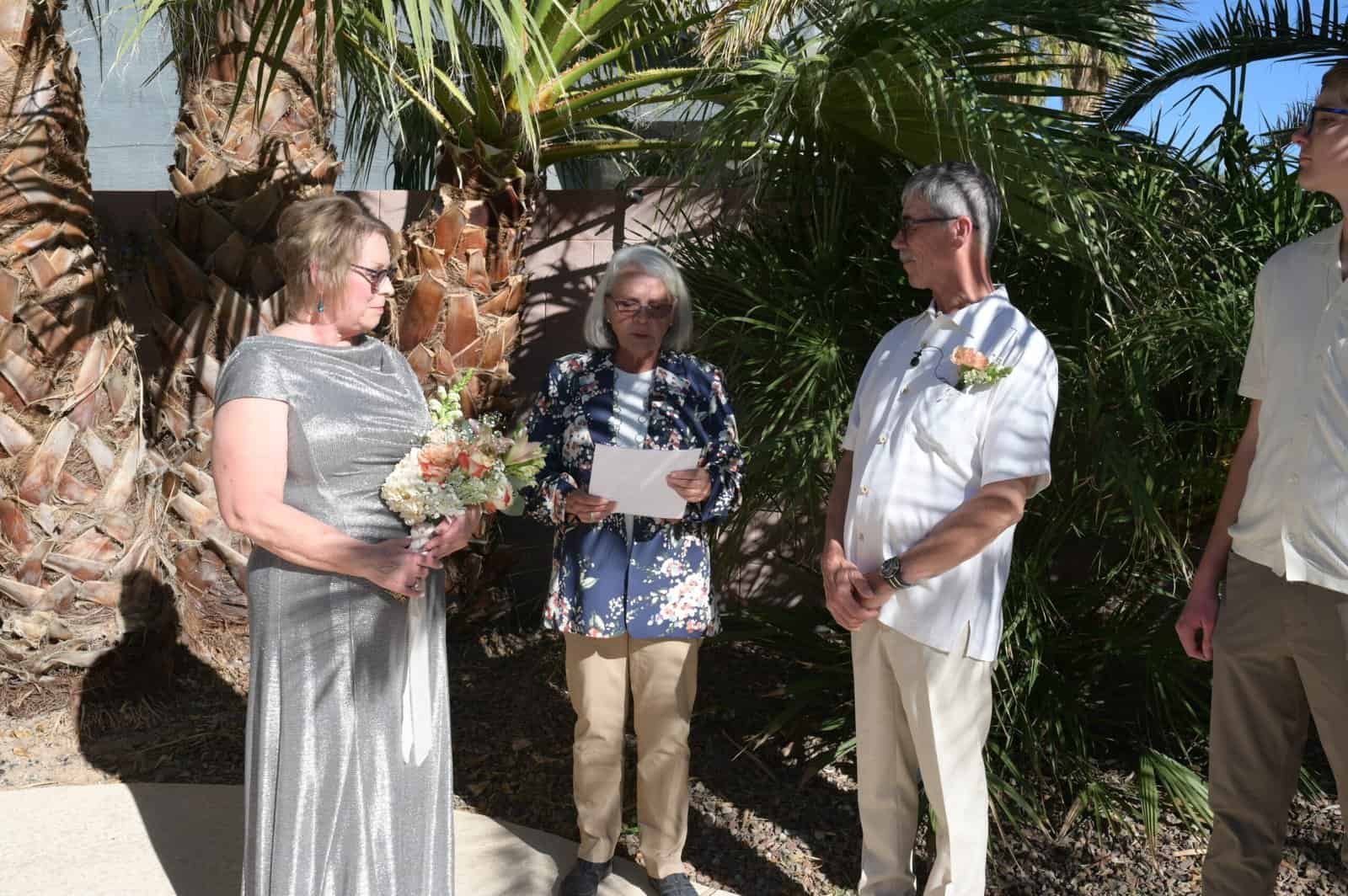 A couple and family members participate in a wedding ceremony outdoors surrounded by tropical plants.