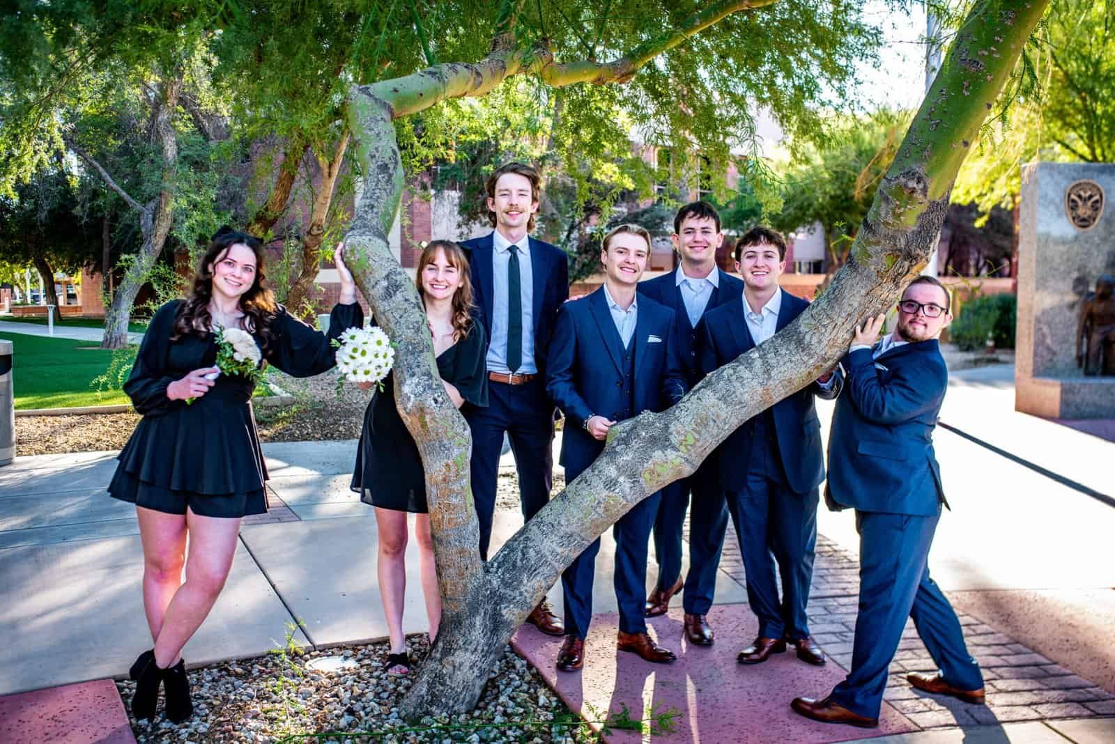 Friends celebrating together outdoors, dressed in formal wear, smiling and having a good time in a park setting.