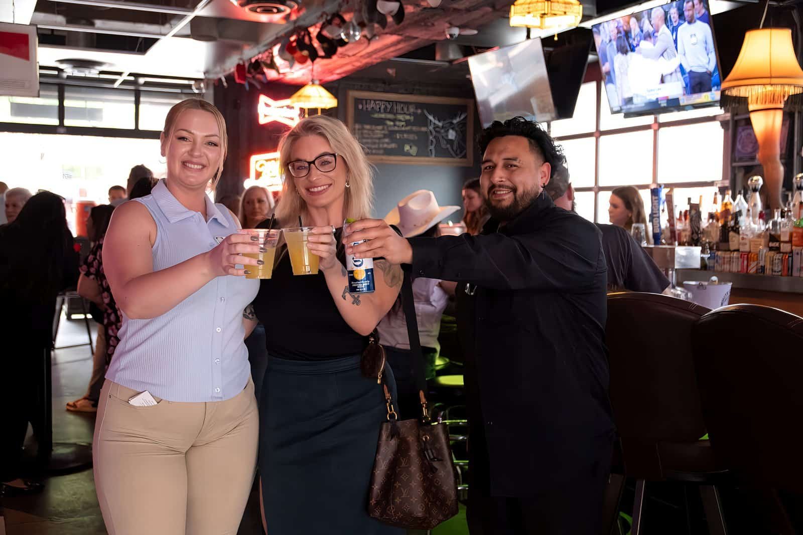 Group of friends smiling and toasting with drinks in a vibrant bar setting.