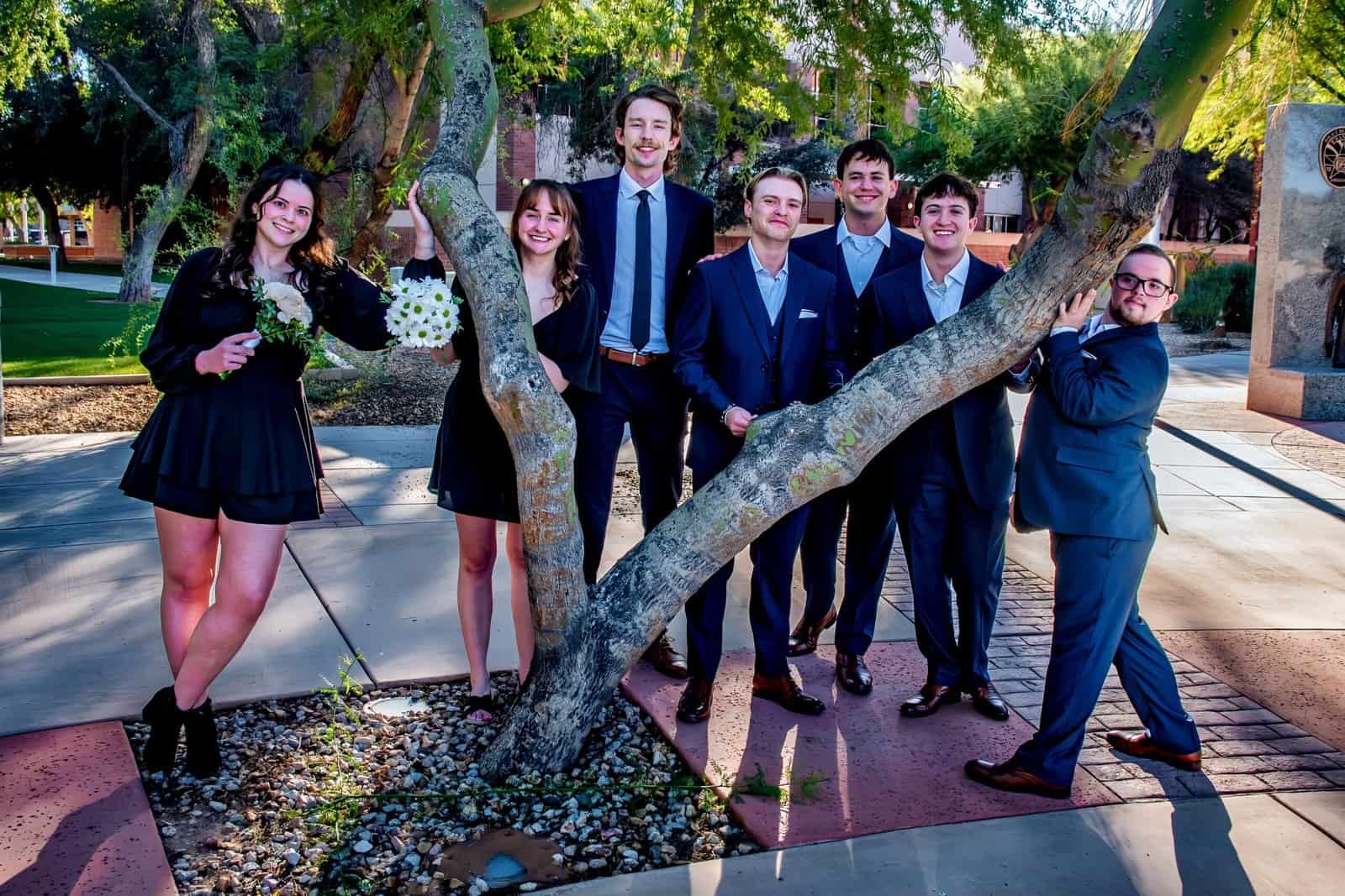 A group of friends dressed in suits and dresses enjoying a sunny day outdoors, smiling and posing for a photo.
