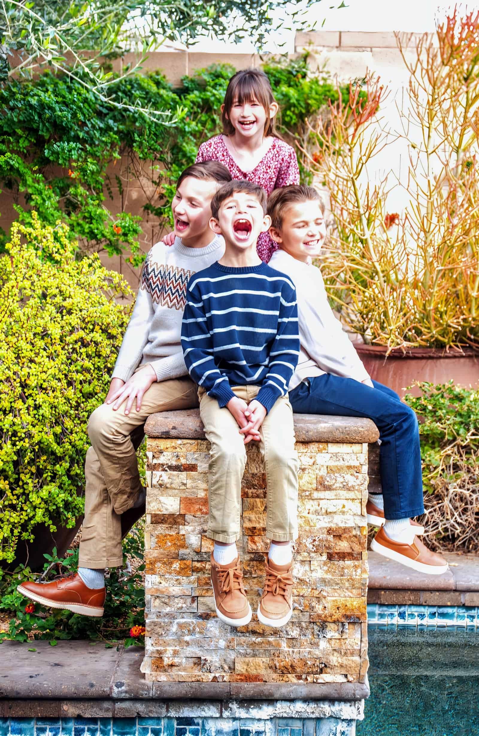 Happy family portrait with kids sitting on a brick ledge near the pool, smiling and having fun in a lush garden setting.
