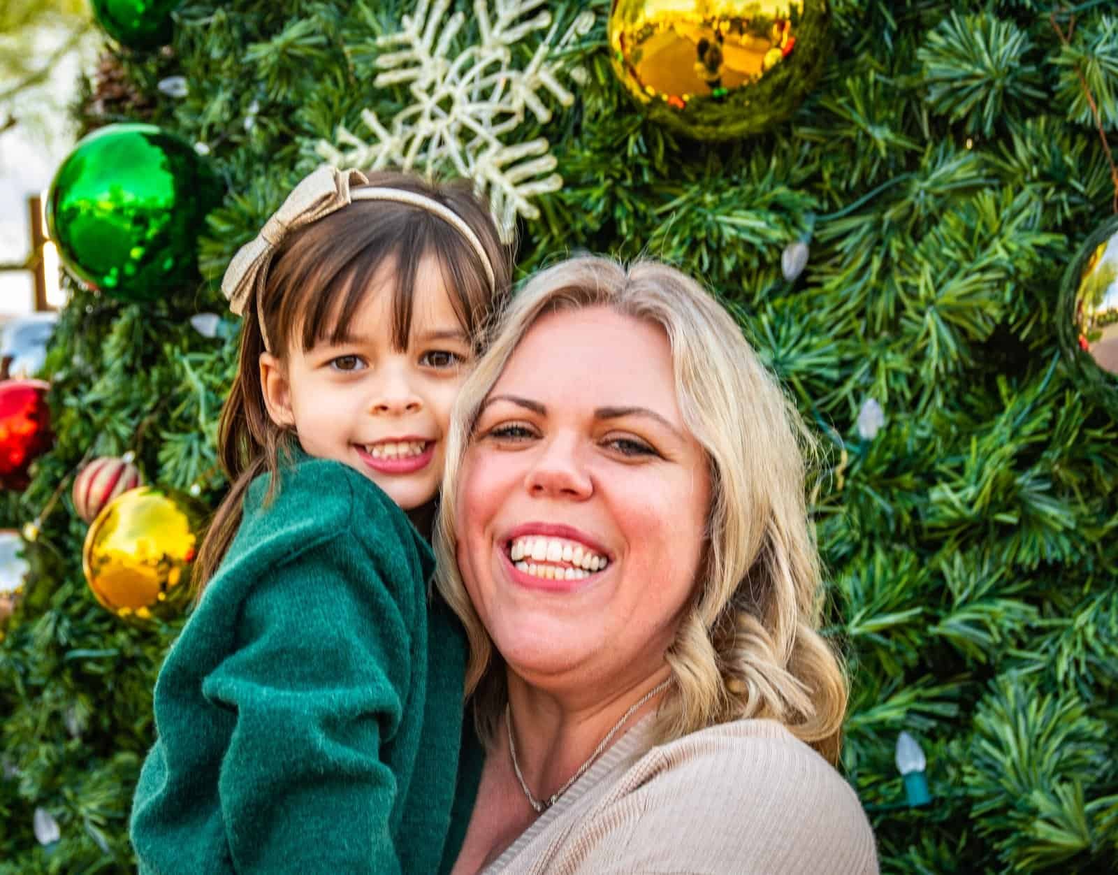 Joyful woman and young girl sharing a festive moment in front of a beautifully decorated Christmas tree.