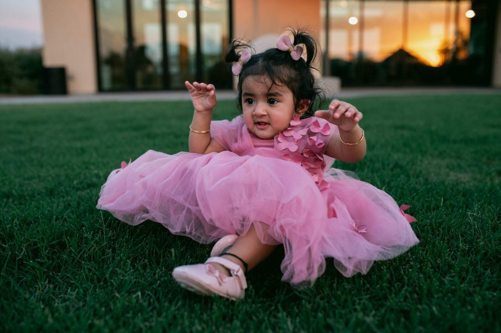 Adorable young girl dressed in a pink tutu, sitting on the grass with a joyful expression, capturing a charming outdoor moment.