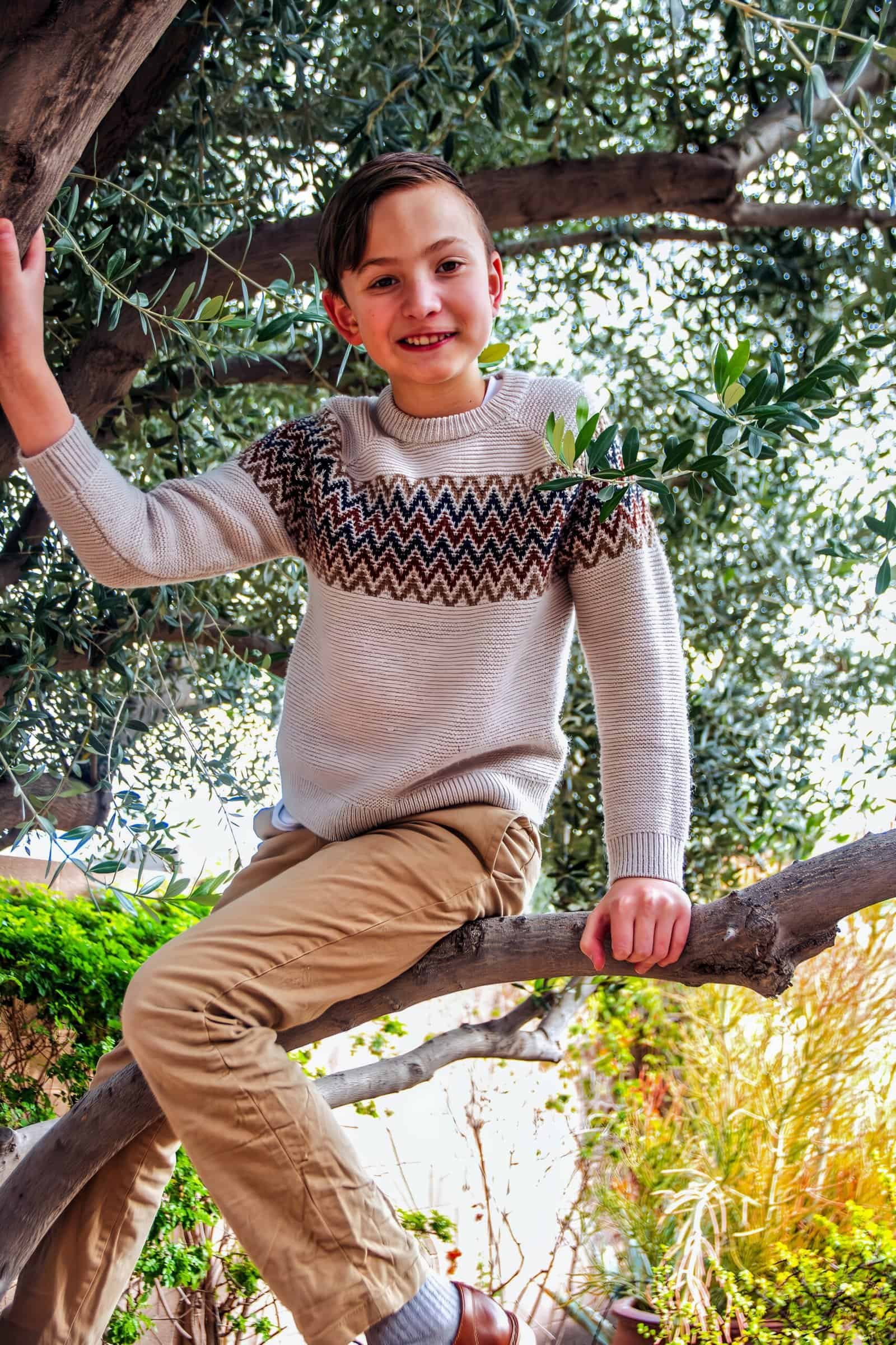 Happy boy enjoying outdoor play on tree branch in a lush garden setting.