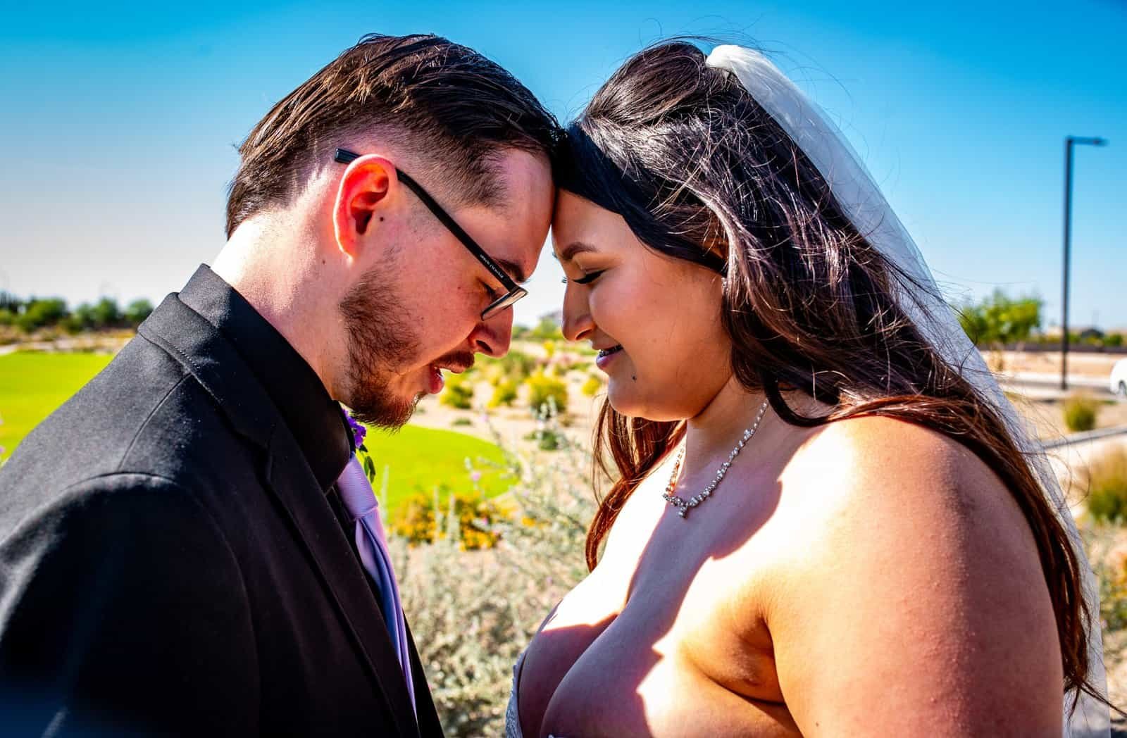 Romantic wedding photo of a bride and groom smiling and touching foreheads outdoors, capturing love and happiness.