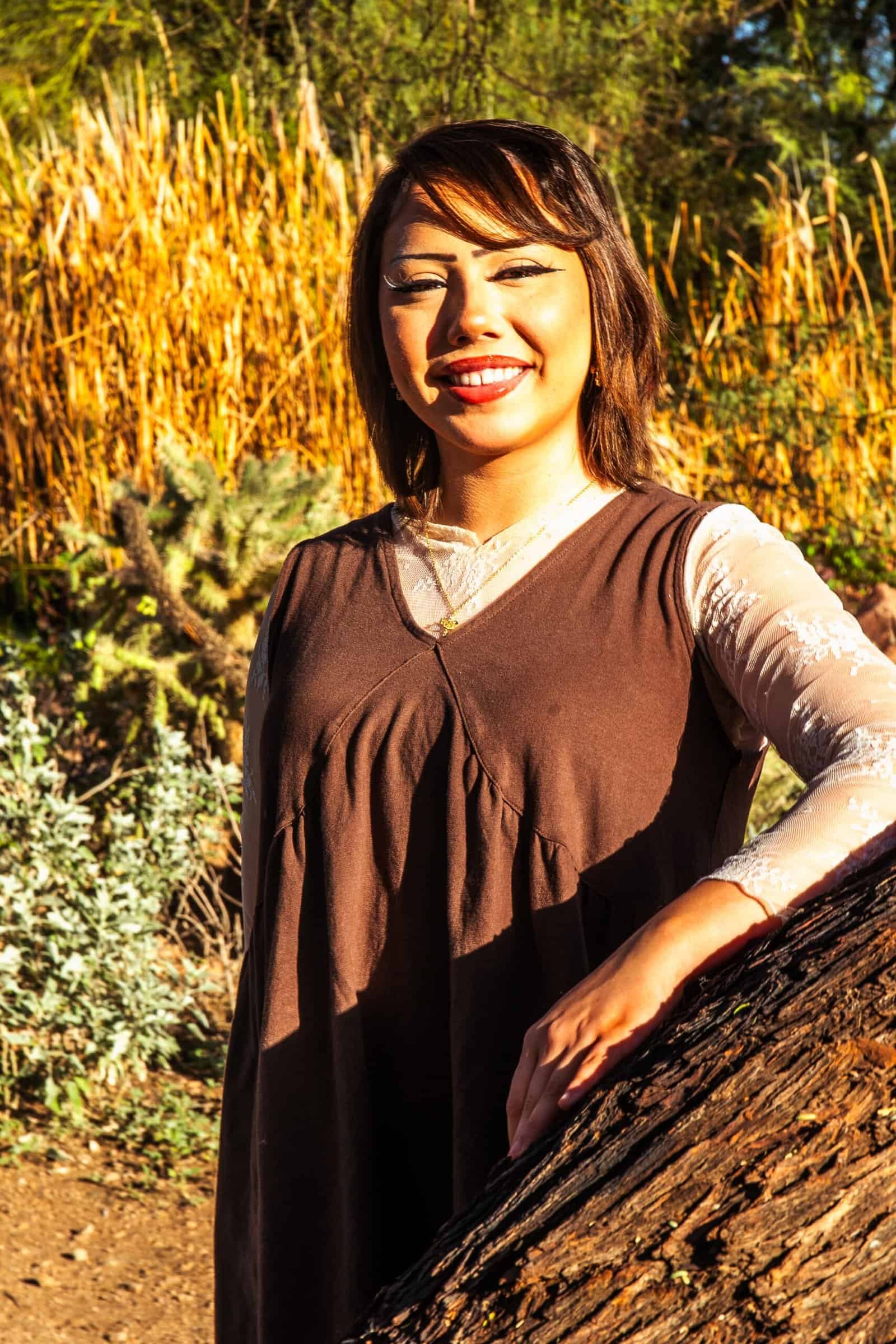 A cheerful woman with a bright smile standing in a vibrant garden or park, capturing joyful moments.