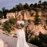 Bridal portrait of a bride holding a bouquet in a scenic canyon landscape during sunset.