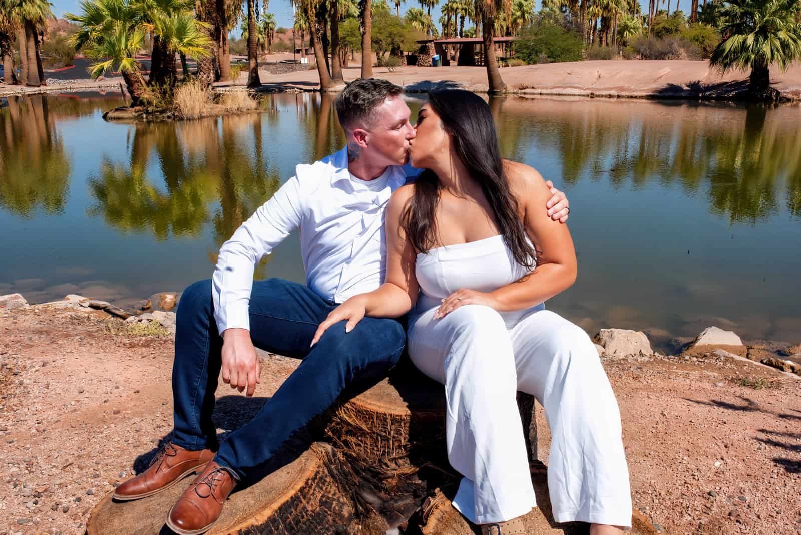 A couple enjoying a tender moment by the water, surrounded by nature and palm trees, perfect for wedding or engagement videos.