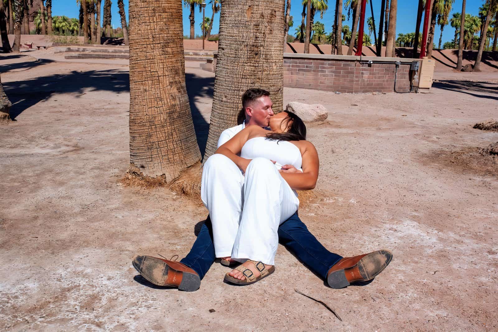 A romantic couple enjoying a tender moment sitting on the sandy beach under palm trees, capturing love and connection.